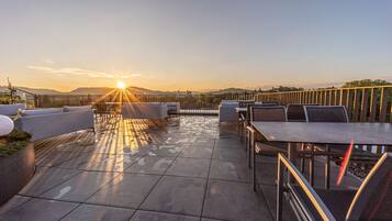 Un patio en la azotea con mesas al aire libre y vistas al atardecer.