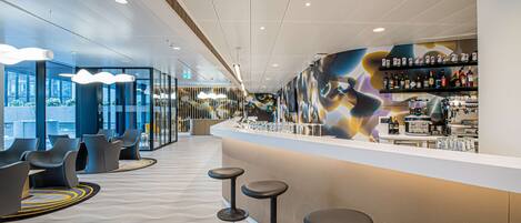 A modern bar area with a counter, stools, and a mural on the wall.