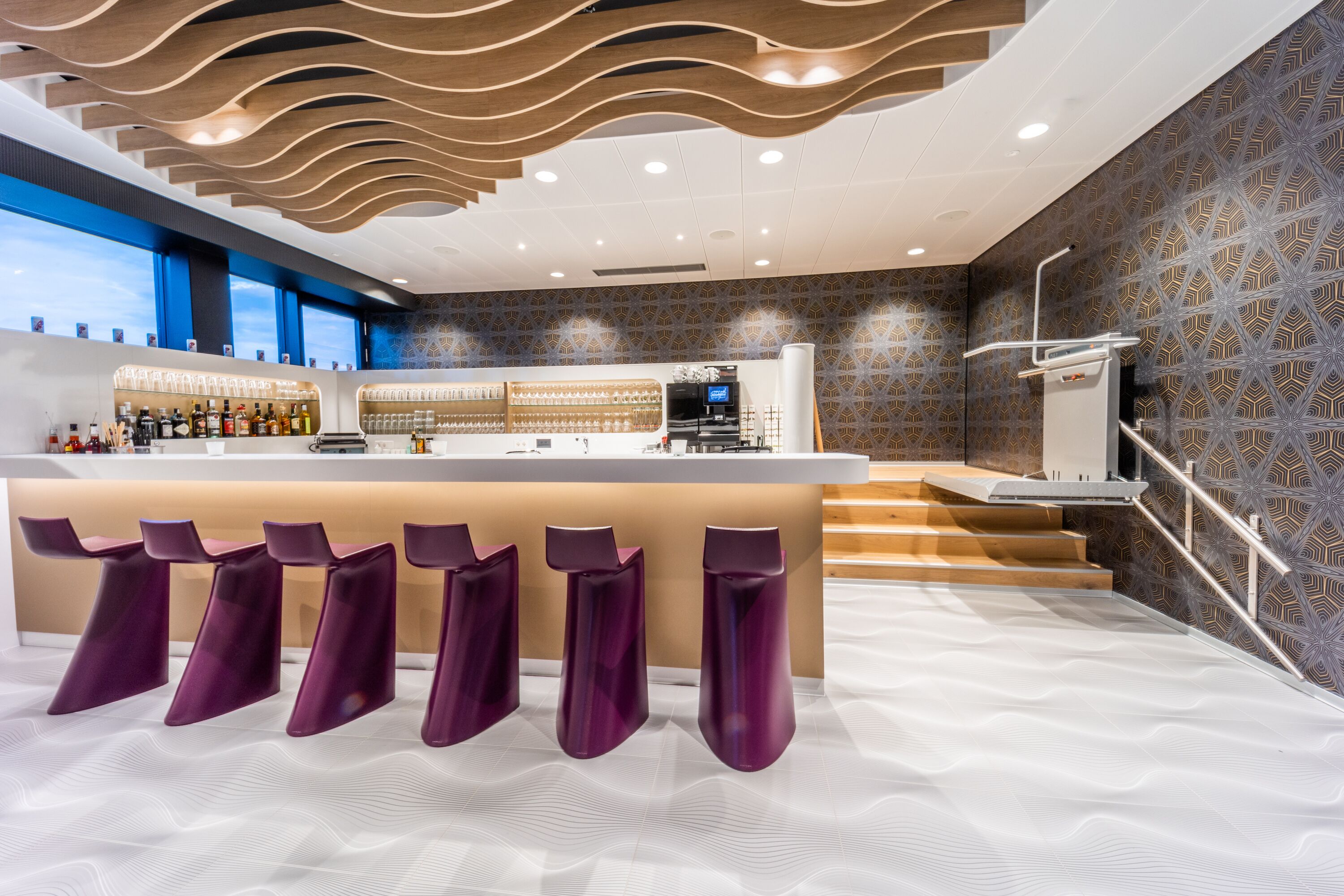 A modern bar area with a long counter, multiple bar stools, and a staircase leading to an upper level.