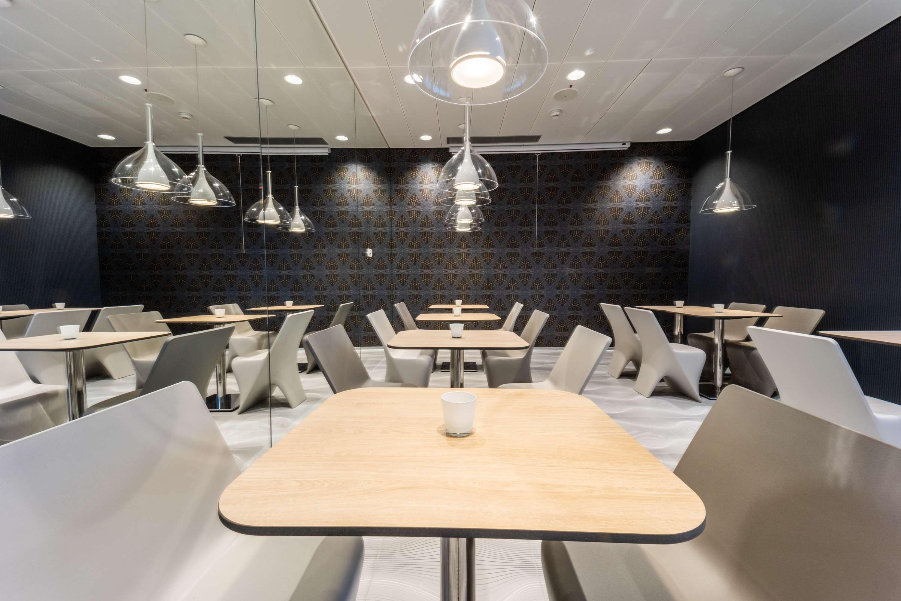 A modern dining area with multiple tables and chairs, pendant lighting, and patterned wall tiles.