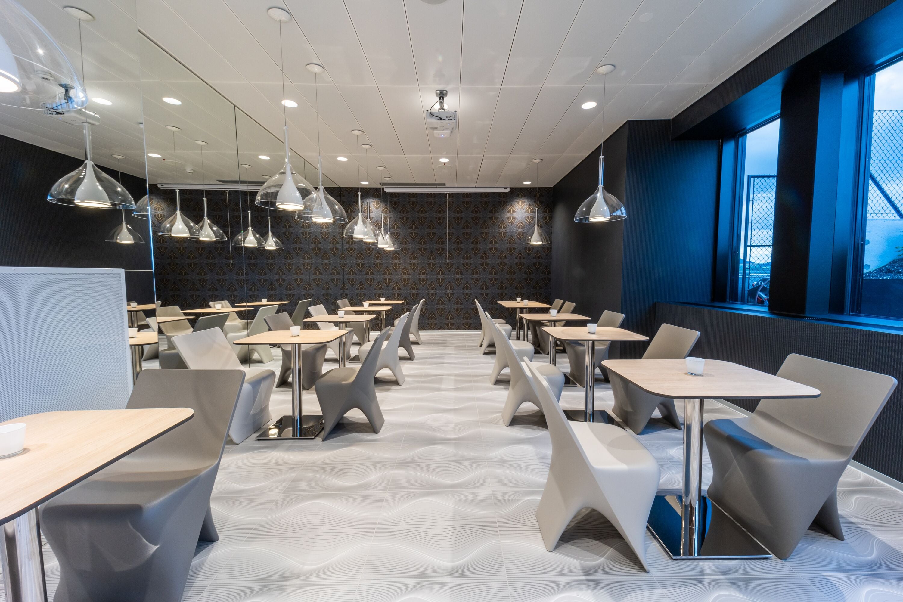 Un'area pranzo moderna con tavoli e sedie, illuminazione a soffitto e pavimento decorato.