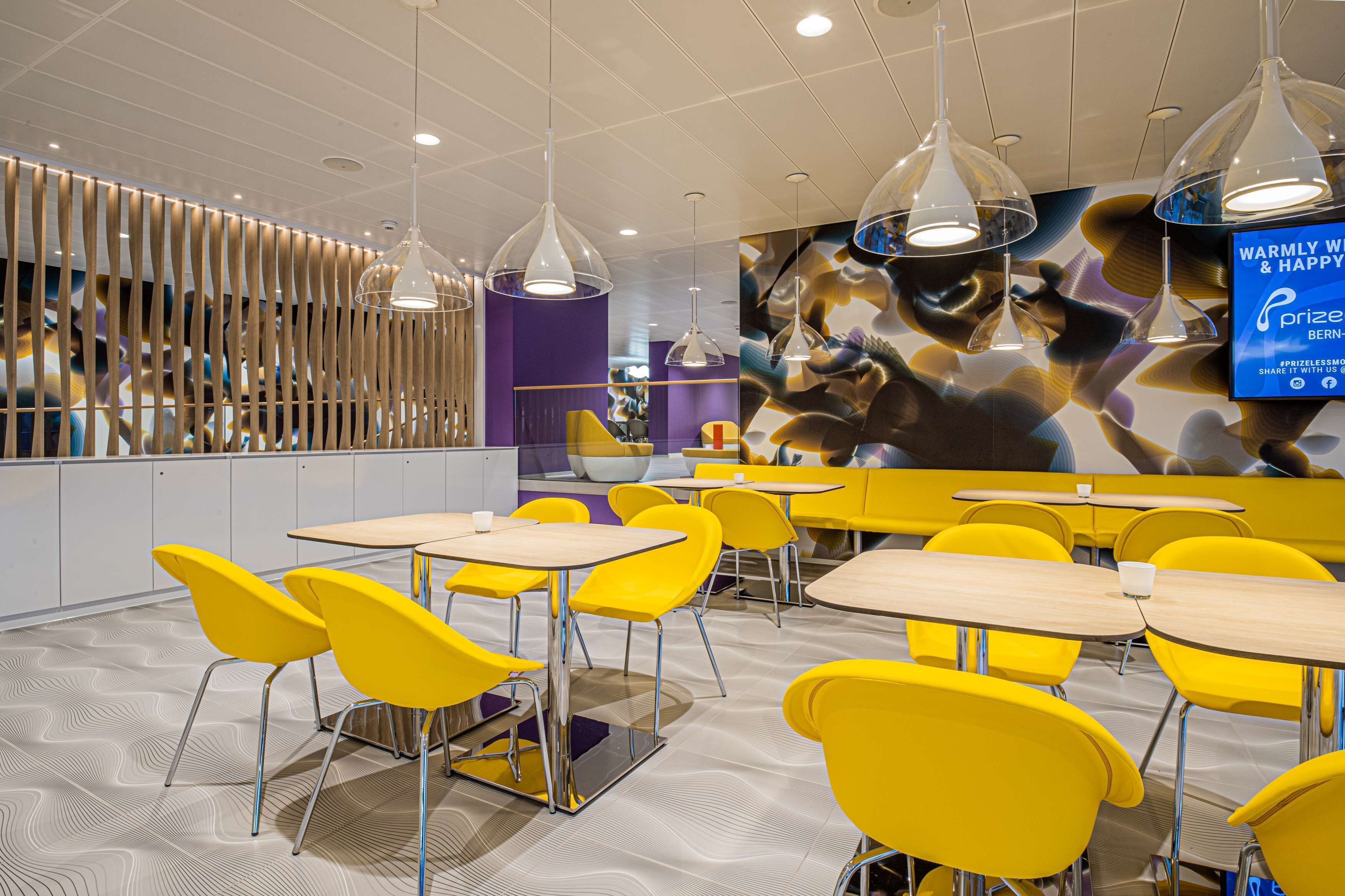 A modern dining area with yellow chairs and tables, pendant lights, and a large mural on the wall.