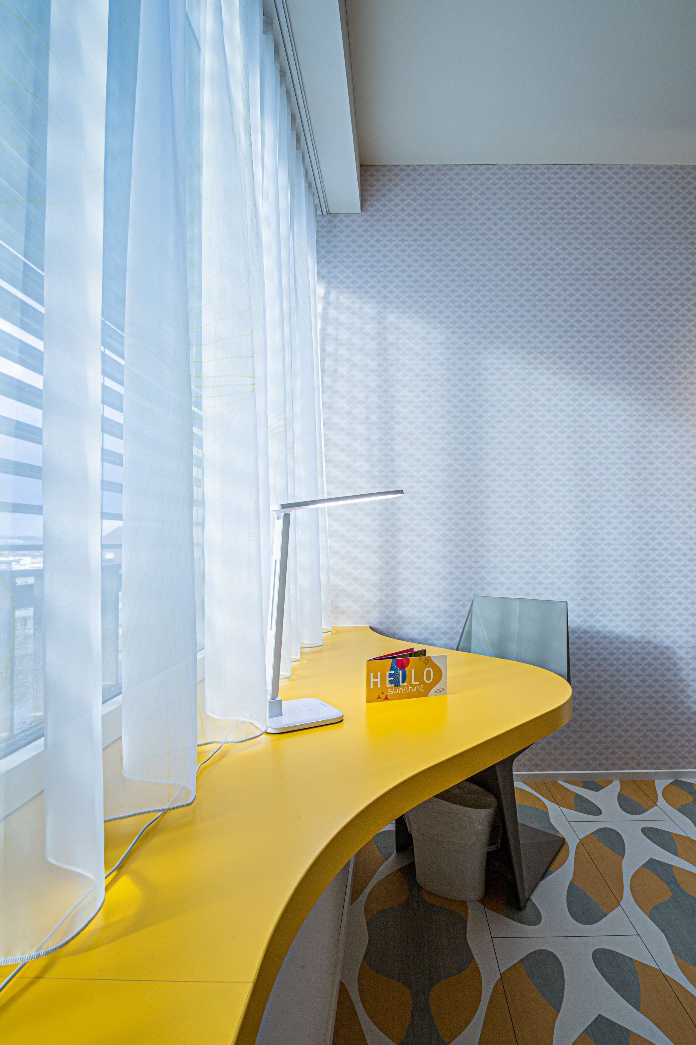 A modern office space with a yellow desk, a white chair, and a desk lamp.