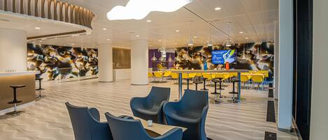 A modern hotel lobby with a reception desk, seating area, and a large digital screen displaying information.