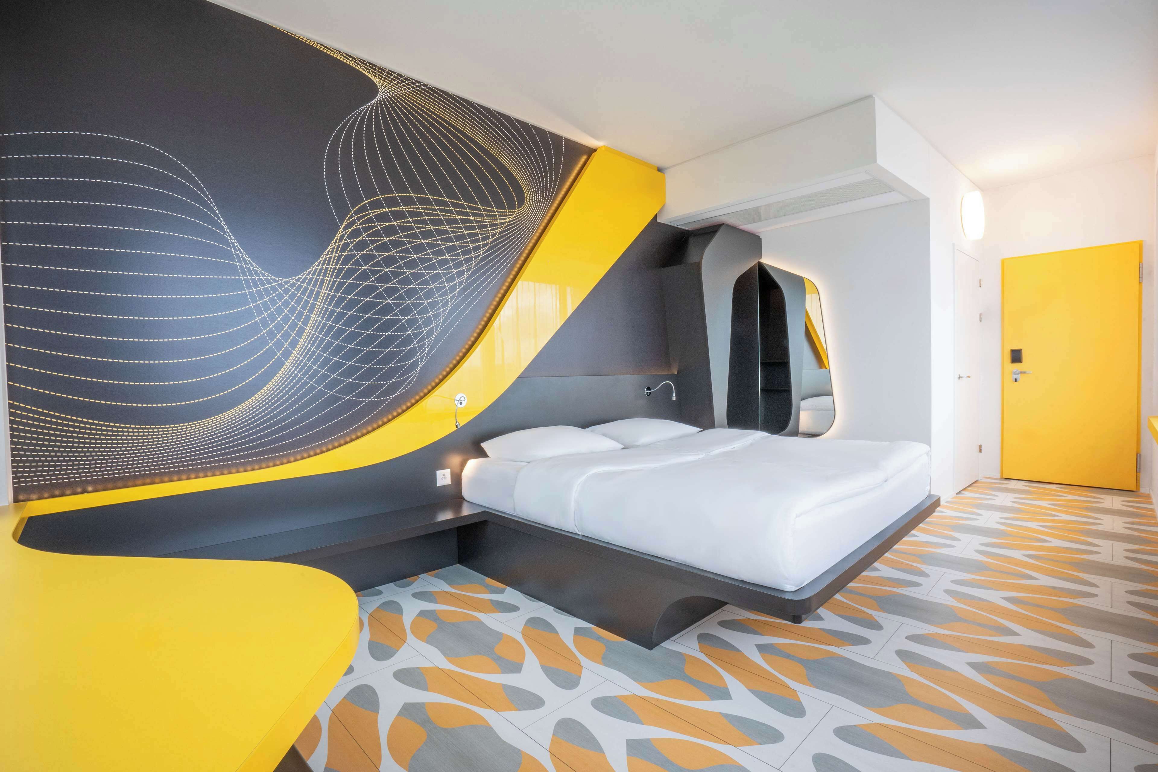 A modern hotel room with a curved bed, a unique wall design, and a patterned floor.