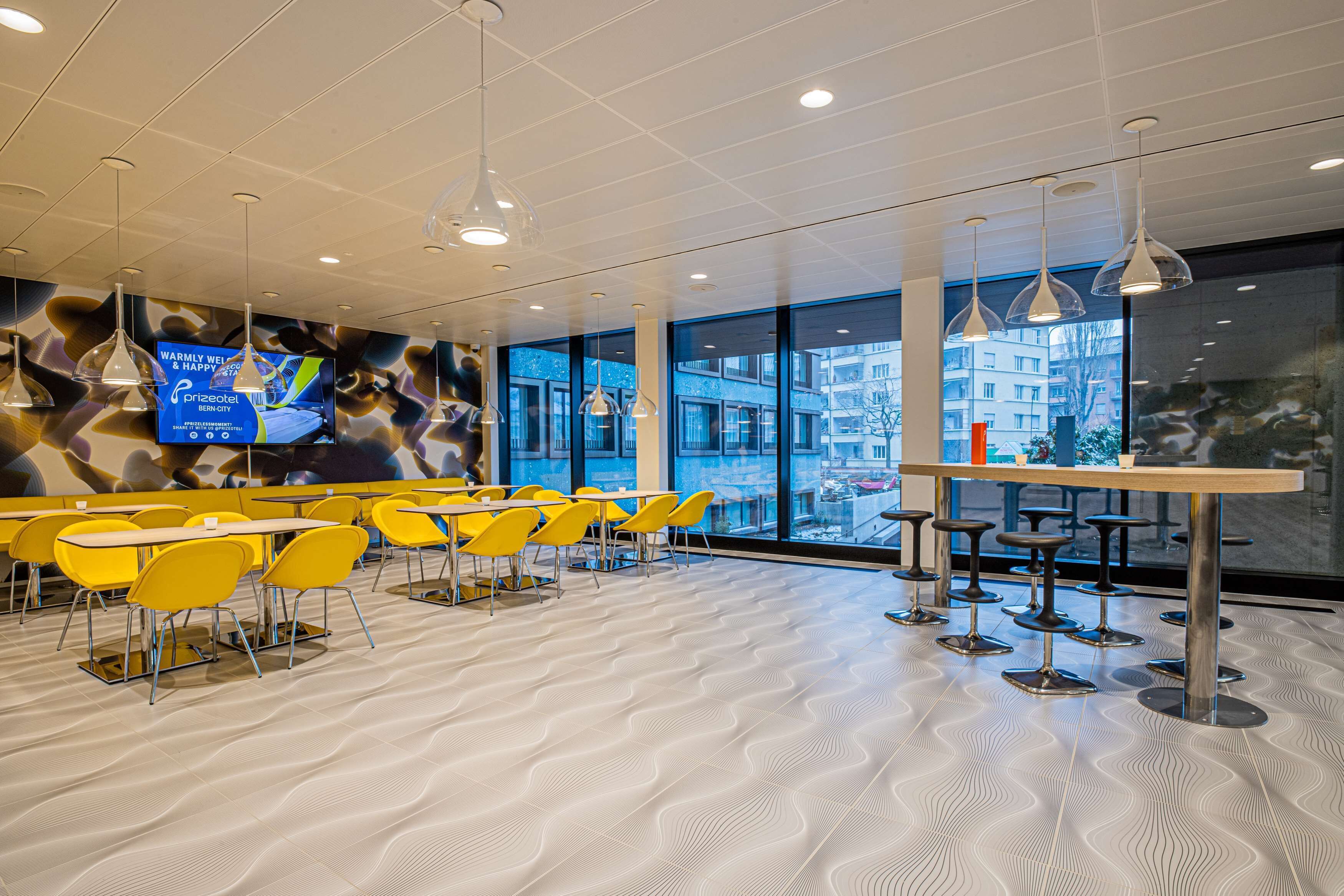 Un espace de restauration moderne avec des chaises et des tables jaunes, un grand écran de télévision et de grandes fenêtres offrant une vue sur la ville.