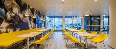 A modern dining area with yellow chairs and tables, a patterned floor, and pendant lighting.