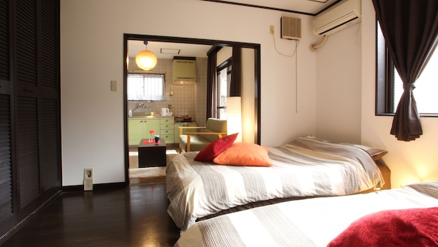 A hotel room with two beds, a sitting area, and a view of the kitchen. - Amenity Apartment (Osaka)