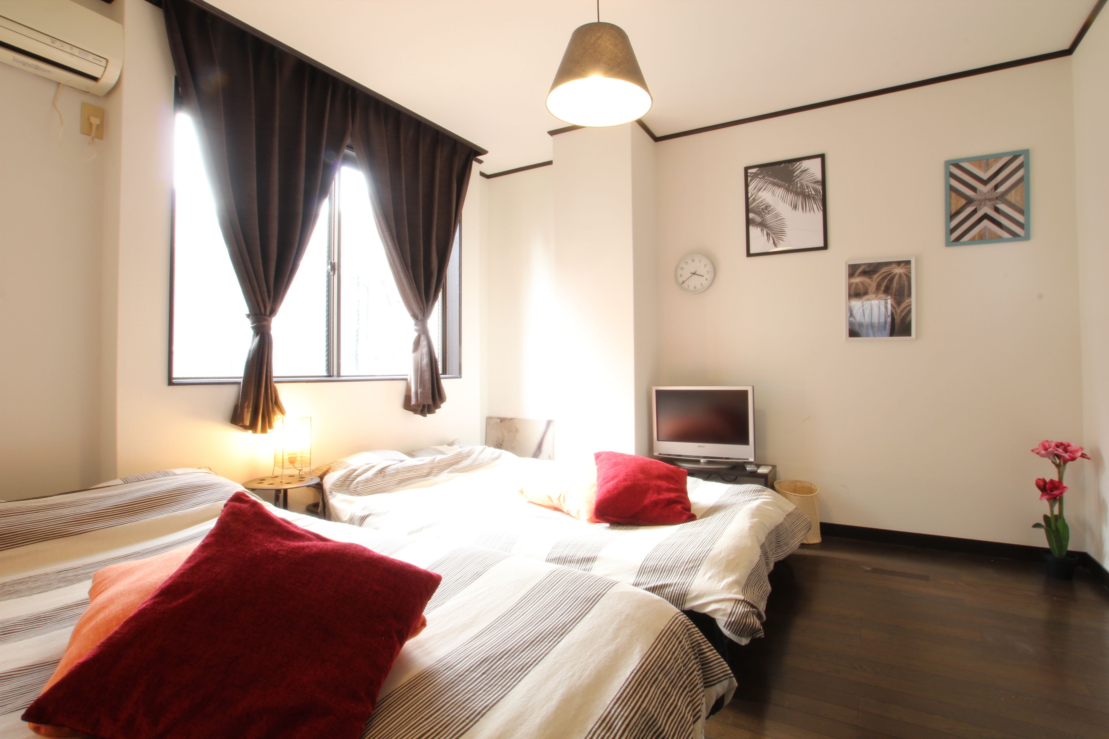 A hotel room with two beds, a TV, a clock, and artwork on the wall.
