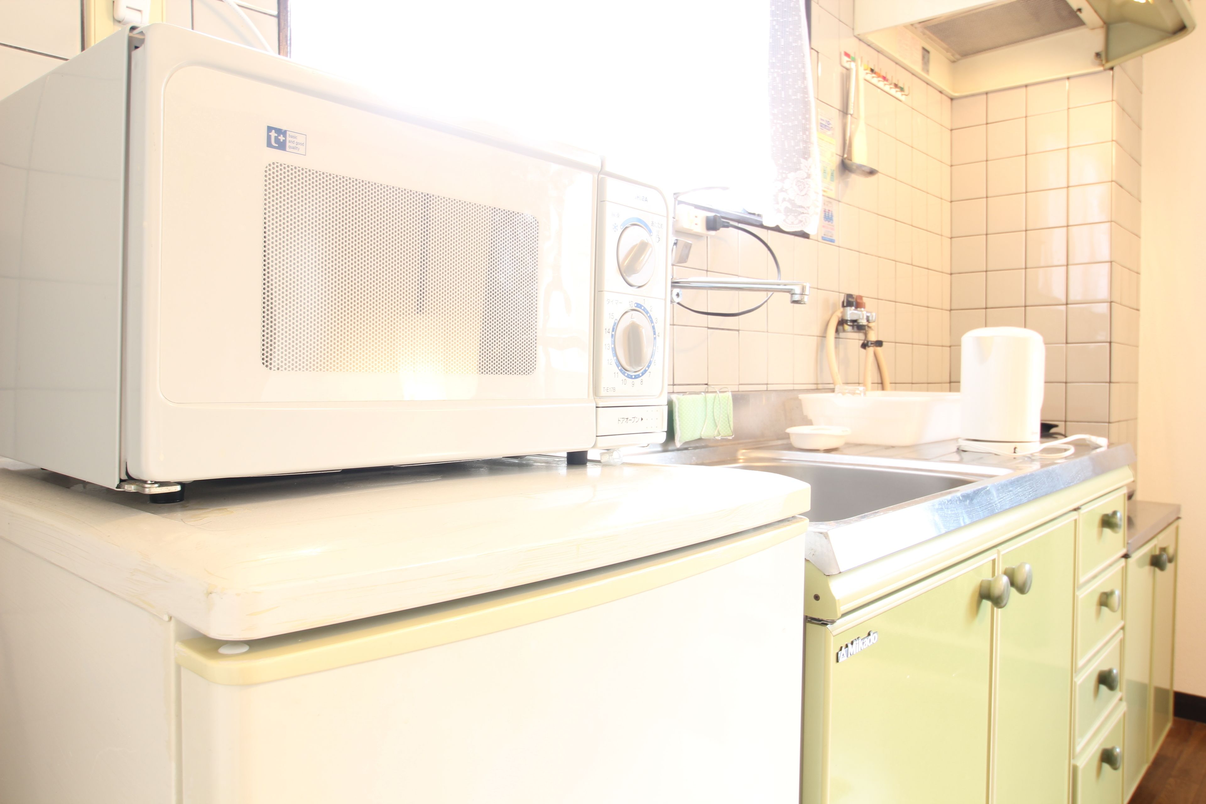 A kitchen with a white microwave on top of a white refrigerator, a sink, and green cabinets.
