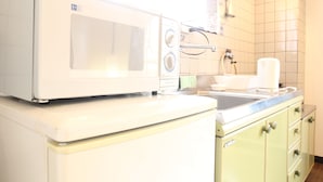 A kitchen with a white microwave on top of a white refrigerator, a sink, and green cabinets. - Amenity Apartment (Osaka)