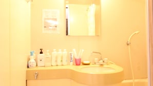 A bathroom with a sink, mirror, and shower. There are toiletries on the sink counter. - Amenity Apartment (Osaka)