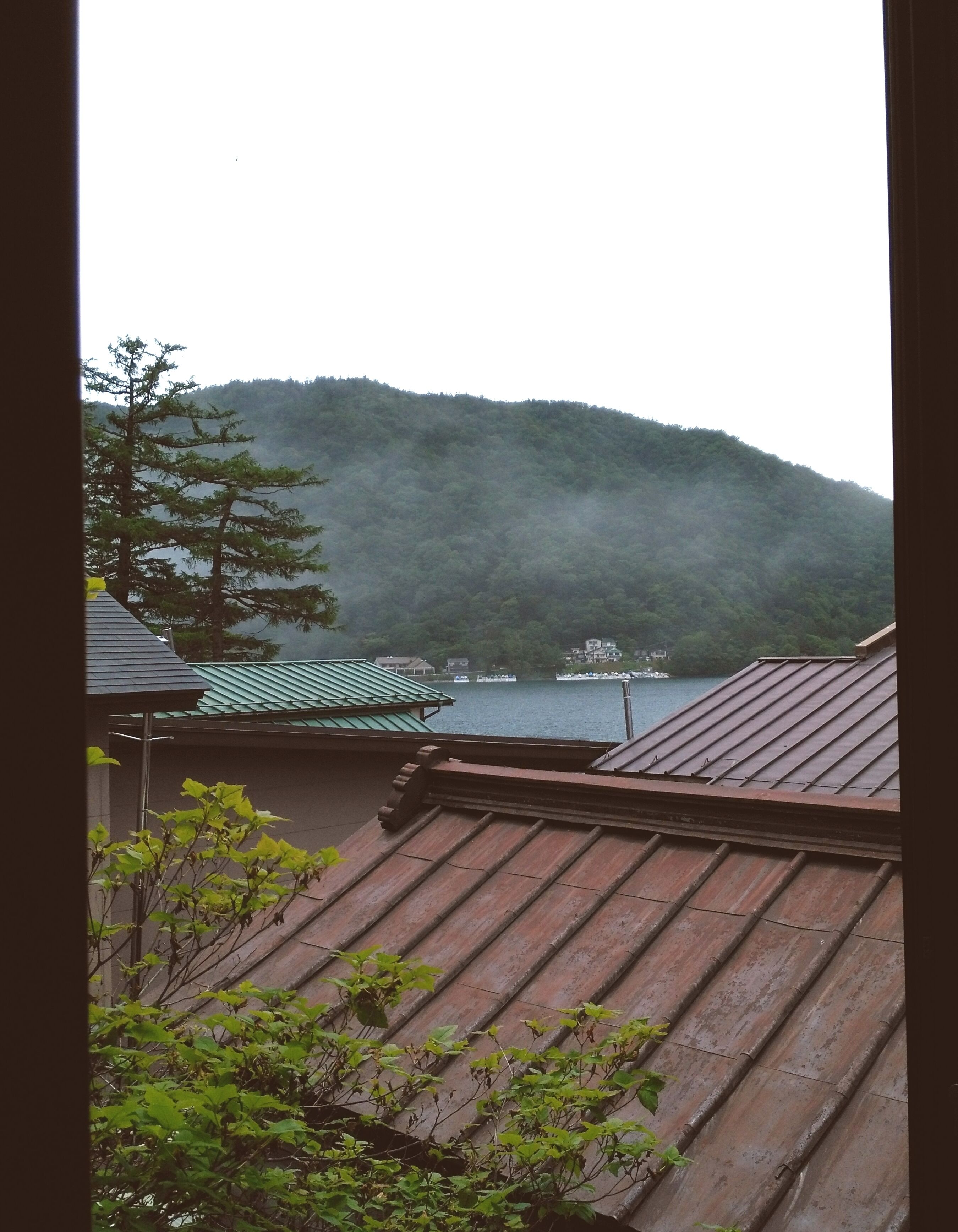A view of a mountain with a lake and boats, and a building with a green roof in the foreground.