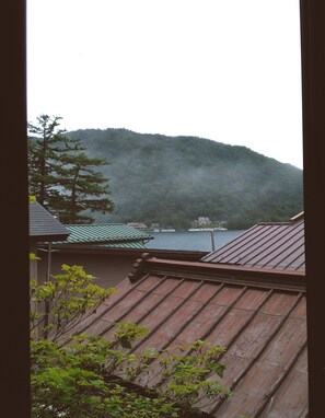 A view of a mountain with a lake and boats, and a building with a green roof in the foreground.