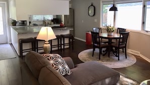 Una sala de estar moderna con un sofá, una mesa de comedor con sillas, una lámpara y una cocina al fondo.