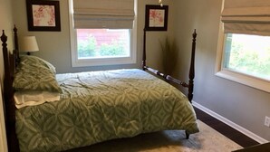 Un dormitorio con cama, ventana con vistas, lámpara y dos cuadros en la pared.