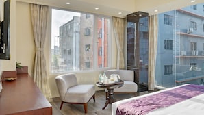 A hotel room with a bed, a chair, a small table with toiletries, and a window with a view of buildings. - Treebo Premium The Crystal, Chinar Park (Barasat)
