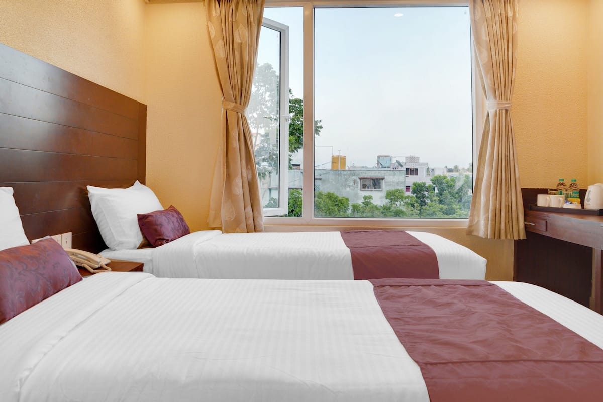 A hotel room with two beds, a wooden headboard, a desk with a chair, and a window with curtains.