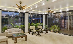 A modern lobby with seating, ceiling fans, and large windows. - Treebo Premium The Crystal, Chinar Park (Barasat)