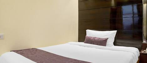 A neatly made bed with a white and purple bedspread, a wooden headboard, and a bedside telephone.