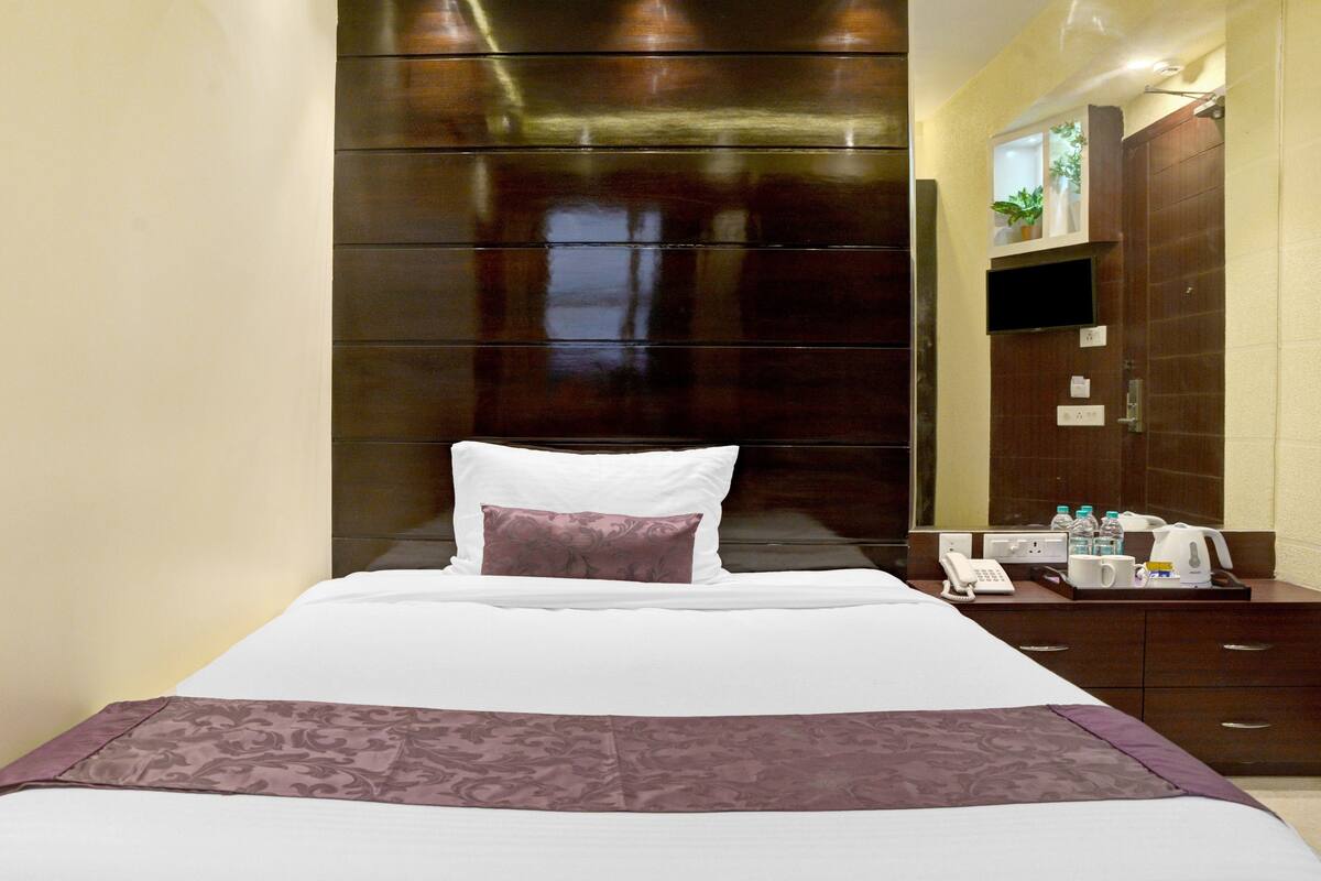 A hotel room with a large bed, a nightstand with a phone and toiletries, and a wall-mounted TV.