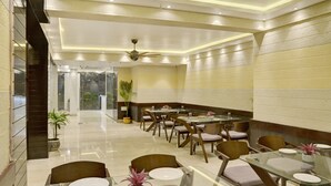 A modern dining area with glass tables and chairs, a ceiling fan, and potted plants. - Treebo Premium The Crystal, Chinar Park (Barasat)