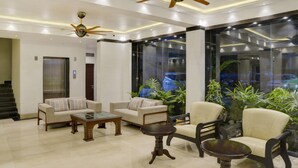 A modern lobby with a seating area, a glass wall with plants, and a ceiling fan. - Treebo Premium The Crystal, Chinar Park (Barasat)