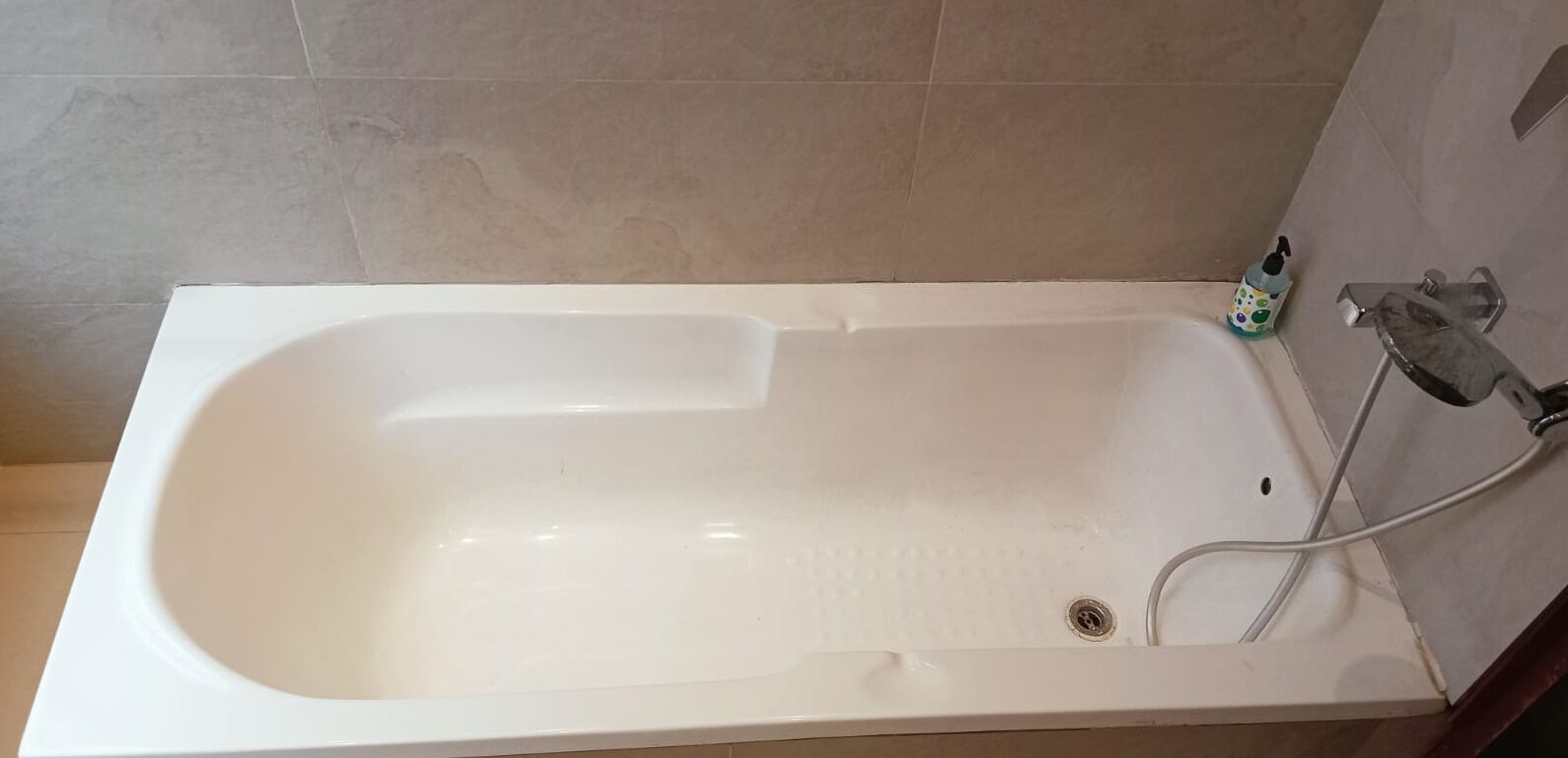 A white bathtub with a handheld showerhead and a drain.