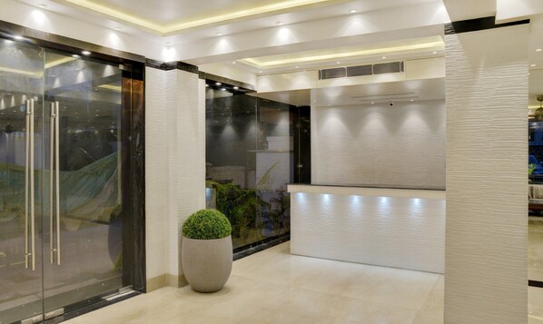 A modern lobby with a glass door entrance, a large potted plant, and a textured wall. - Treebo Premium The Crystal, Chinar Park (Barasat)