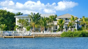 A waterfront property with a large house, a dock, and palm trees.