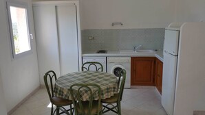 A compact kitchen with a dining area, including a table with chairs, a washing machine, and a refrigerator. - Mini-villa No. 10 - 2/4 people (Porto-Vecchio)