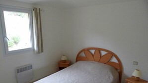 A single bed with a wooden headboard, two bedside tables with lamps, a window with curtains, and a wall-mounted heater. - Mini-villa No. 10 - 2/4 people (Porto-Vecchio)