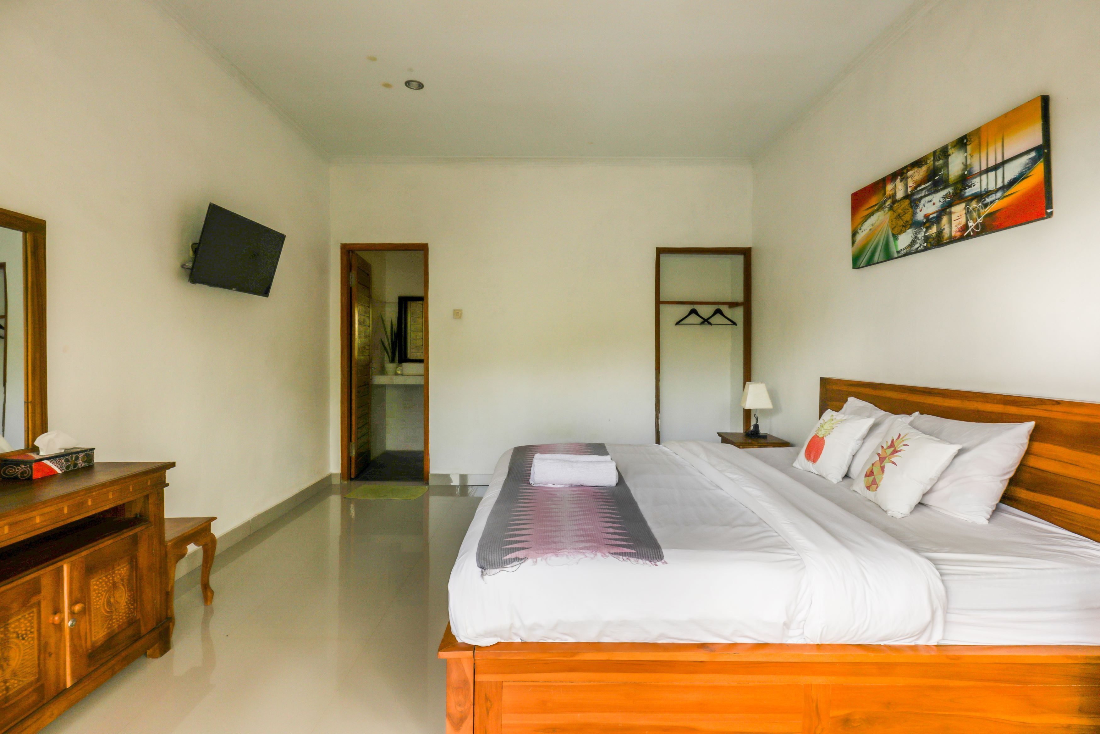 Une chambre d’hôtel avec un lit en bois, du linge de lit blanc, un téléviseur à écran plat fixé au mur et un tableau au-dessus du lit.