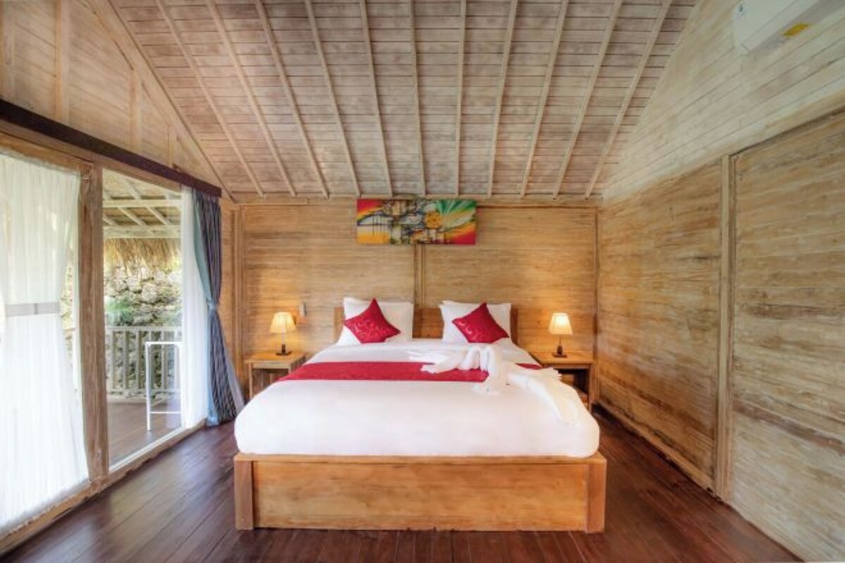 A wooden-framed room with a bed, two bedside lamps, and a view through a glass door.