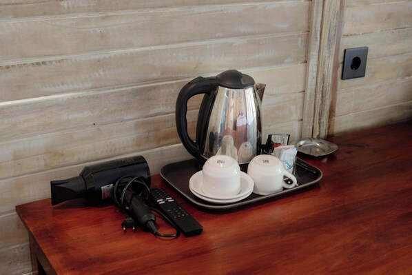 Una mesa de madera con una tetera, dos tazas, una bandeja, un control remoto y un adaptador de corriente.