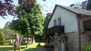 Una casa con balcón, un patio con mesa y sillas, y una escultura en el jardín.
