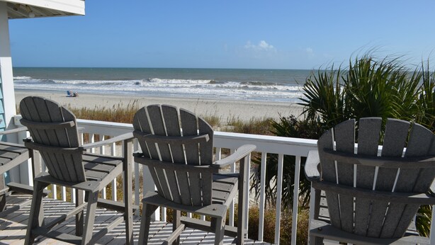 Une terrasse avec trois fauteuils Adirondack donnant sur une plage.