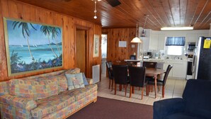 L’intérieur chaleureux d’un chalet avec un coin repas en bois, un canapé coloré et une cuisine équipée du strict nécessaire.