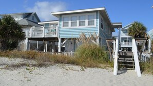 Une propriété située en bord de mer, avec une maison bleue, une terrasse en bois et un escalier menant à un balcon.
