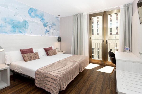 Habitación de hotel con cama, mesita de noche, escritorio, silla y vistas al exterior.