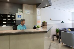 A reception area with a counter, a desk, a chair, a sofa, and a small table with a plant.