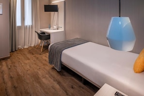 Una habitación de hotel con cama, escritorio, silla, televisión y una lámpara moderna.