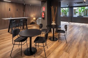 A modern interior with a bar area, round tables, and chairs, a fire extinguisher, and a plant. - Hostal Opera Ramblas (Barcelona)