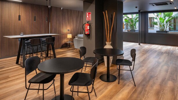 A modern interior with a wooden wall, a bar area, and round tables with chairs.
