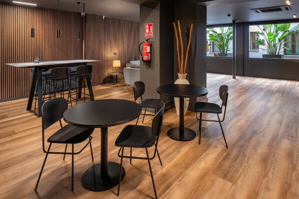 A modern interior with a wooden wall, a bar area, and round tables with chairs.