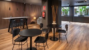 A modern interior with a wooden wall, a bar area, and round tables with chairs. - Hostal Opera Ramblas (Barcelona)