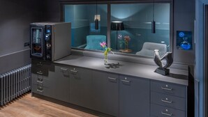 A modern kitchen with grey cabinets, a built-in microwave, and a window with a view of a blue chair and a vase with flowers. - Hostal Opera Ramblas (Barcelona)