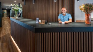 A reception desk with a modern design, featuring a wooden panel wall, pendant lighting, and a vase with flowers. - Hostal Opera Ramblas (Barcelona)