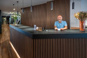 Un mostrador de recepción de diseño moderno, con un panel de pared de madera, iluminación colgante y un florero con flores.