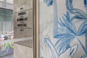 Una pared con el texto 'EST. OPERA RAMBLAS HOSTAL 1971' y una parte de un mural tropical con motivos azules y blancos.